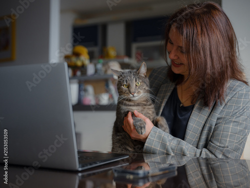 Mother working remotely from home, caucasian woman with her cat using laptop at home. Smart working and smart studying with pet
