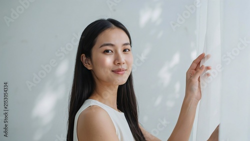 Young asian woman with long dark hair standing by a white curtain