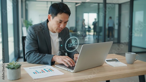 Asian man working on laptop with digital clock and finance in office