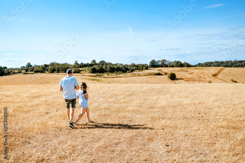 Father and daughter walking through dry grass field
