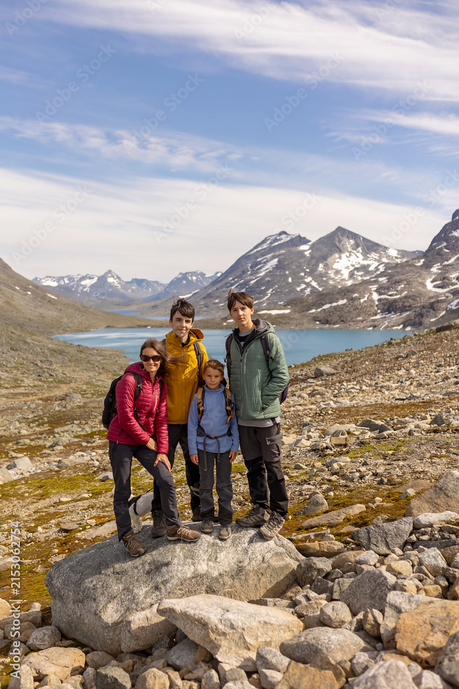 Fototapeta premium Beautiful european family with children and pet dog, hiking Kyrkja mountain on a beautiful sunny summer day, sunset, snow, lakes, valley