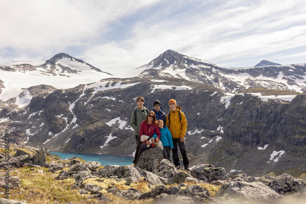 Fototapeta premium Beautiful european family with children and pet dog, hiking Kyrkja mountain on a beautiful sunny summer day, sunset, snow, lakes, valley