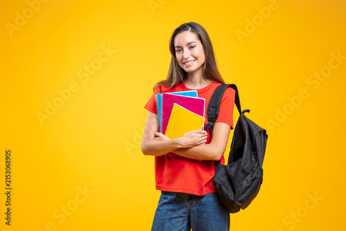 Smiling student carrying backpack and notebooks on yellow background