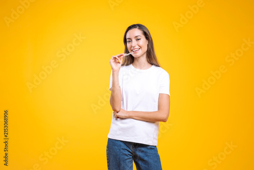 Young woman smiling, holding clear dental aligner on a yellow background