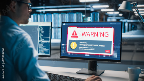 Male II Specialist in Glasses Faces a Critical Virus Alert on His Desktop Monitor, Reading a Red System Compromised Warning Pop-up While Working in a Modern Data Center Office.