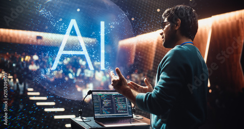 Male Lecturer Delivering a Computer Science AI Keynote From a University Podium, Gesturing to Activate Hologram. Laptop Code SHows as the Auditorium Audience Follows Machine Learning Software Concepts
