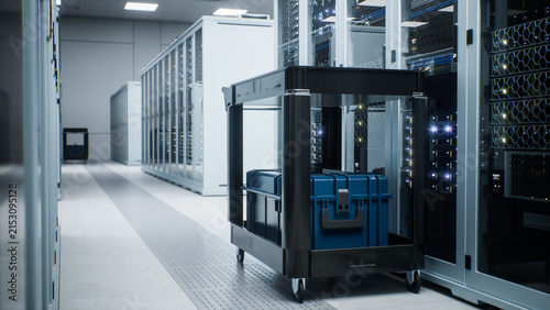 Modern Data Center with Wheeled Maintenance Trolley Loaded With Hard Cases and Tool Boxes Parked Beside an Open Rack Bay in a Narrow Data Center Aisle, Awaiting Hardware Servicing of Ai Compute Nodes.