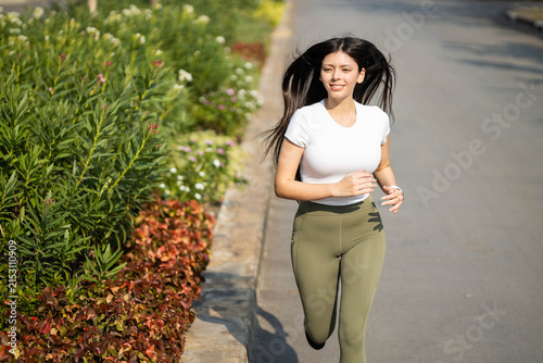 Fotografie Young woman running on a paved path next to green foliage, actively exercising t