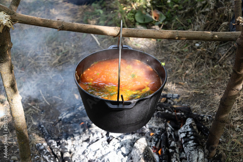 Delicious traditional Ukrainian red borscht soup cooking in a cast iron pot outdoors on fire, stirred with a ladle, showcasing fresh vegetables and rich broth for camping and nature travel food.