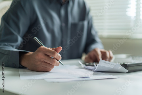 Close-up of office worker holding pen writing on financial document and checking bills at desk.