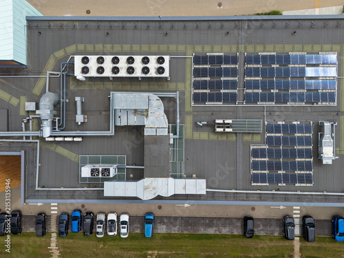 Aerial top-down view of commercial rooftop with solar panels and HVAC cooling units beside parking lot, building energy infrastructure and sustainability concept.