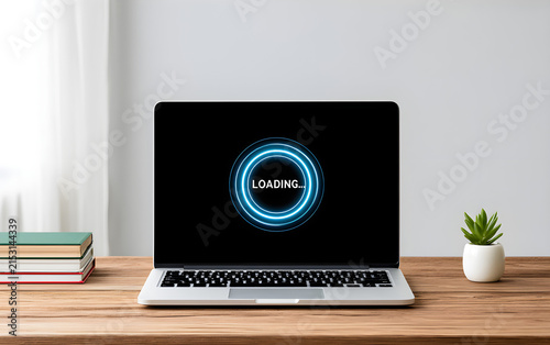 Modern laptop displaying a blue loading spinner and text on its screen placed on a wooden desk next to a stack of books and a potted succulent waiting progress process buffering