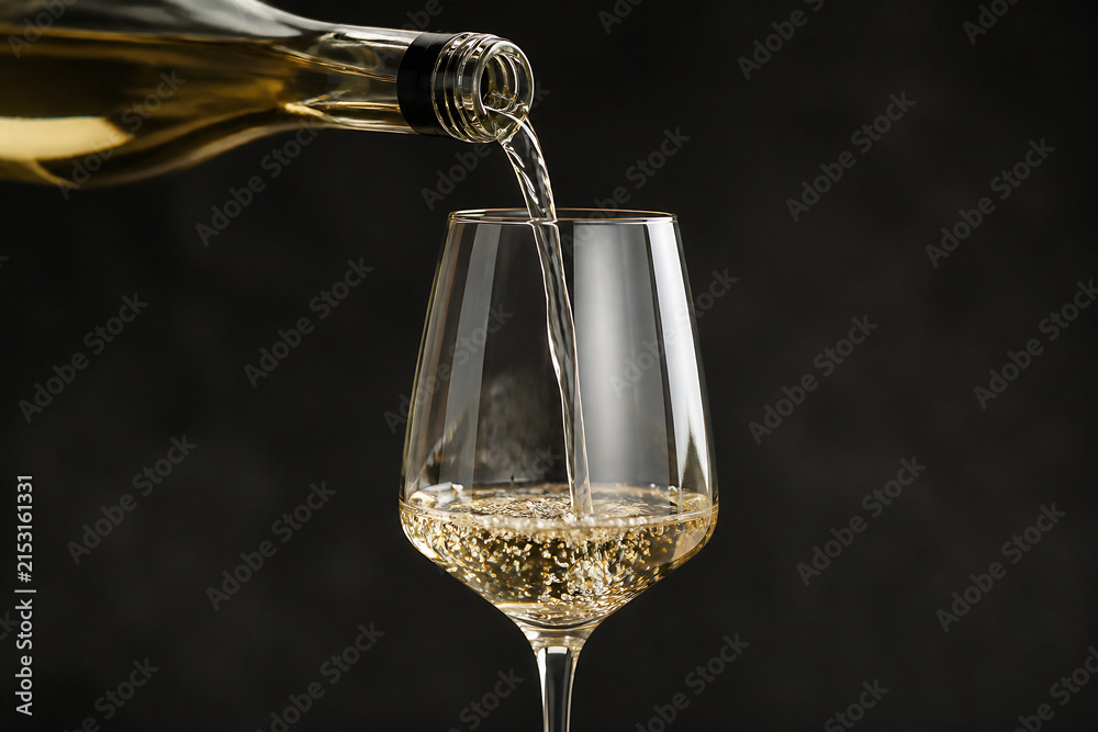 Obraz premium A stream of golden liquid is being poured from a bottle into a wine glass against a dark background.