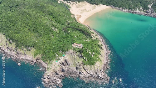 Drone footage captured orbiting Mui Dien Lighthouse and Bai Mon Beach in Dak Lak (formerly Phu Yen) Province, Vietnam. The aerial view reveals the iconic lighthouse, crescent-shaped sandy beach, and s