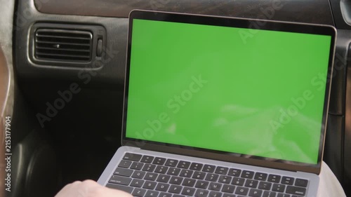 Laptop with green screen inside car. Hand holds device, focused on work. Ideal for travel, remote jobs, or digital editing. Clean, modern setup with natural car interior lighting