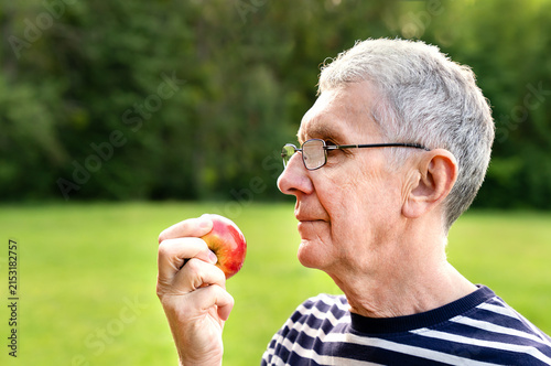 Senior man holding a fresh apple outdoors. Healthy eating, nutrition and an active lifestyle in older age. Copy space. Selective focus.