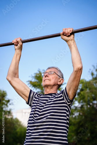Senior man exercising on a horizontal bar outdoors, representing strength, fitness, active aging and a healthy lifestyle. Copy space.