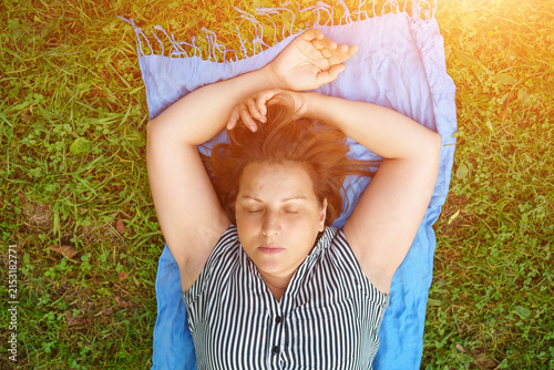 Canvastavla Top view of a mature caucasian woman lying with closed eyes on a blue blanket on summer grass, ideal for outdoor rest, picnic and relaxation content
