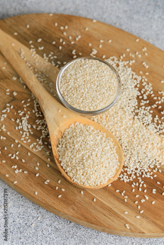 Fotografie Sesame seeds on a wooden spoon and board with a glass bowl filled with seeds in