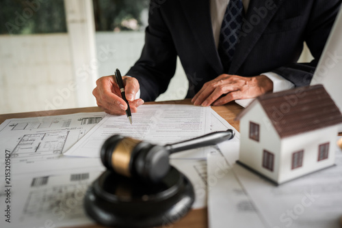 Принти на полотні Real estate professional reviewing property documents at a desk with a house model, legal gavel, architectural plans, laptop, and scales, representing property law and transactions