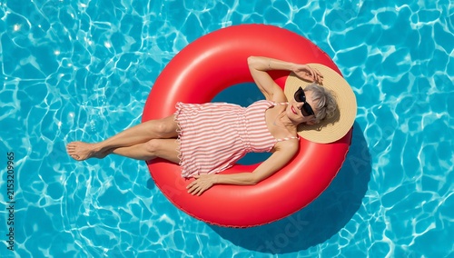 Woman relaxing on a red inflatable ring in a swimming pool on a sunny day