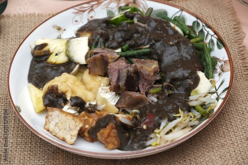 Foto Plate of rujak cingur, a traditional Indonesian specialty served with dark petis sauce, vegetables, tofu, and sliced ingredients on a patterned plate