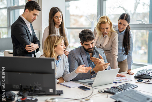 Business team gathered around laptop discussing project and financial reports at desk in office.