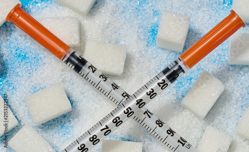 Fotografie Two insulin syringes crossed over cubes and scattered white sugar on a blue back