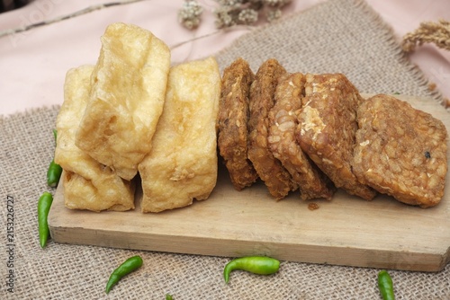 Foto Indonesian fried tofu and tempeh served on a wooden board with green chilies and rustic burlap background
