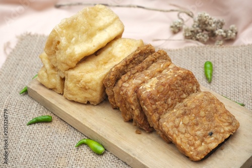 Foto Indonesian fried tofu and tempeh served on a wooden board with green chilies and rustic burlap background