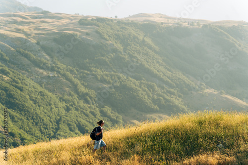 Female traveler walking on green hill slope, admiring epic landscape view. Small person big nature concept