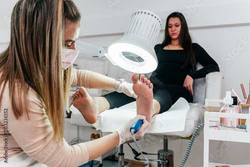 Specialist wearing protective mask and gloves applying antiseptic spray to a client's feet during a clinical podiatry consultation and hygiene treatment.