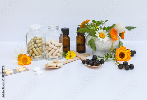 Two wooden spoons—one with natural, vitamin-rich blackcurrant berries, the other with capsules of dietary vitamin supplements. Alternative medicine, folk remedies for health care