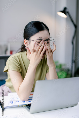 Fotografie Young asian business woman experiencing eye strain and fatigue from prolonged co