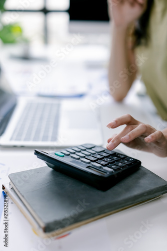 Person's hands using a calculator to manage personal finances and business accounting, calculating expenses, income, and taxes on an office desk with a laptop and documents