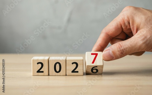 Hand flipping a wooden block to change the year from 2026 to 2027
