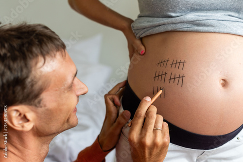 Принти на полотні Man marking tally lines on pregnant woman's belly in close-up