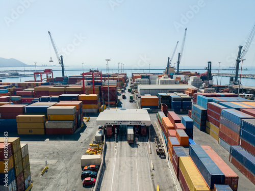 Quadro su tela Aerial drone view of a container terminal entrance gate with trucks, port check-in checkpoint, colorful shipping containers, cranes and sea background for global logistics and trade concept