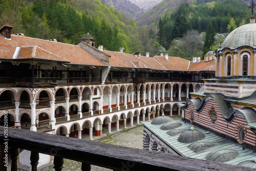 Obraz na plátně The Rila Monastery, a UNESCO World Heritage site in Bulgaria, showcases its stunning architecture with arched colonnades and domed roofs, set against a backdrop of lush green mountains