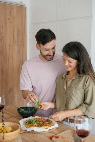 Happy couple making homemade pizza together in kitchen at home