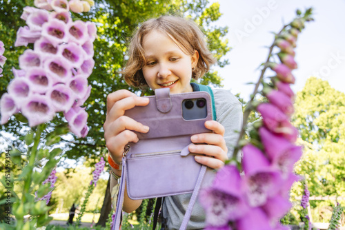Smiling girl photographs purple foxglove flowers with a smartphone