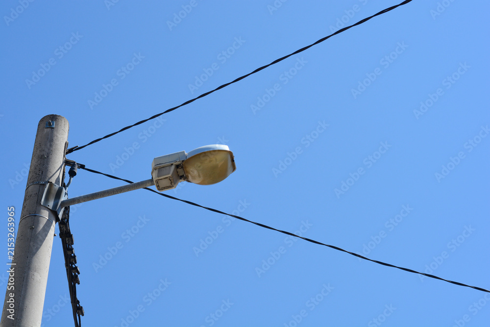 Obraz premium An old street lamp mounted on a concrete utility pole is surrounded by power lines under a clear blue sky.