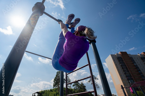 Bild auf Leinwand young female is engaged in physical exercises on a crossbar, hanging upside down
