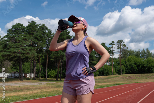 Принти на полотні young female at the stadium, sweaty and tired, drinks water from a bottle to que