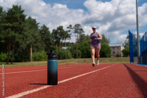 Fotografie young female is running at the stadium, tired and sweaty, running to a bottle to