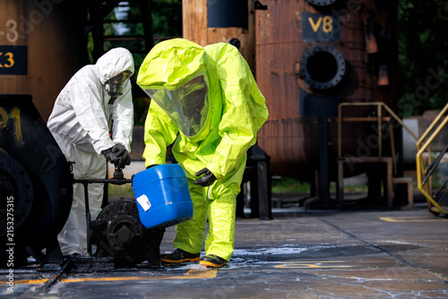 Hazmat workers in protective suits handle a chemical container during hazardous material response training