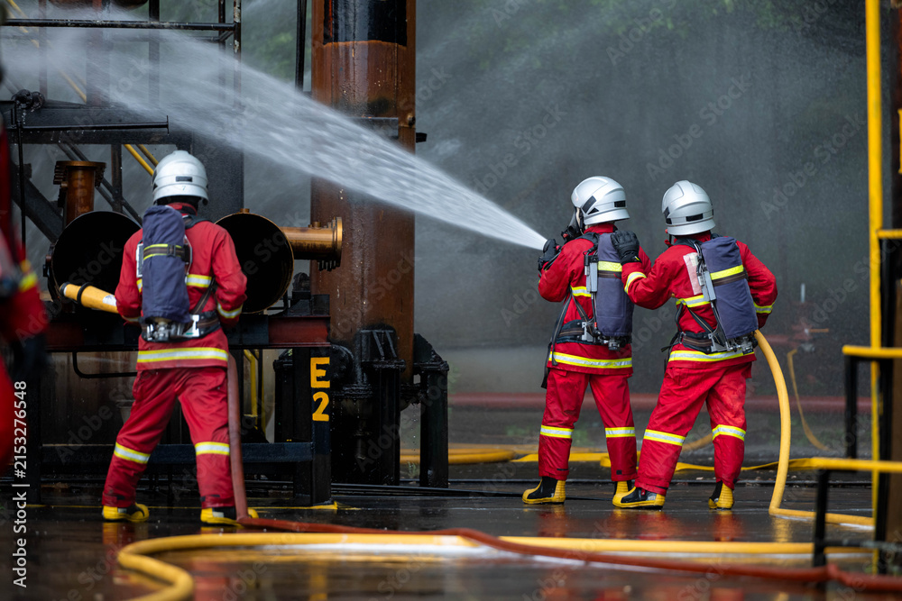 Naklejka premium Firefighters use water hoses to control flames during a coordinated industrial fire