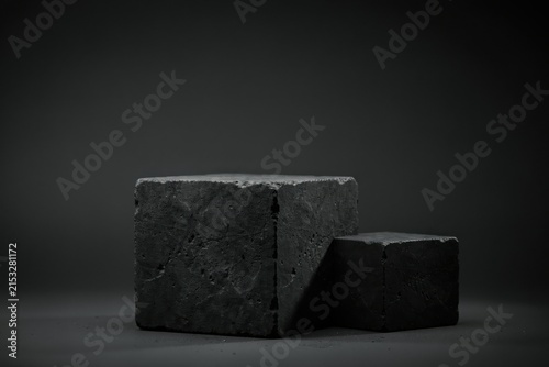 Two dark gray stone cubes of different sizes placed on a dark surface, featuring a rough texture and dramatic studio lighting setup