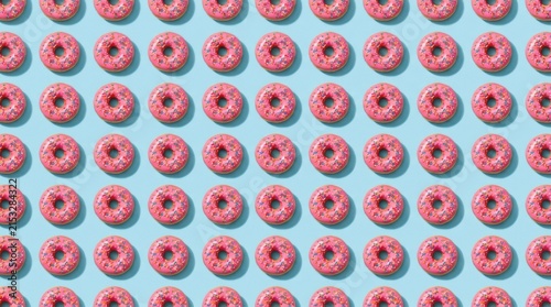 Delicious pink frosted donuts with colorful sprinkles arranged in a uniform pattern on blue background