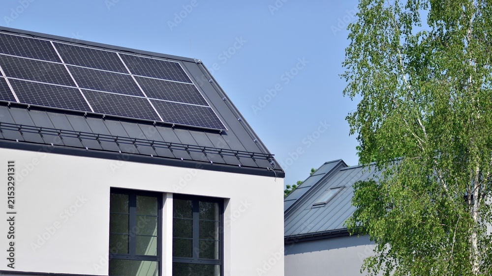 Fototapeta premium Modern Home with Rooftop Solar Panels and Green Trees Under Blue Sky